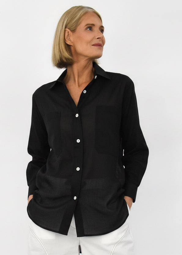 Woman wearing a black shirt with white buttons on a plain background