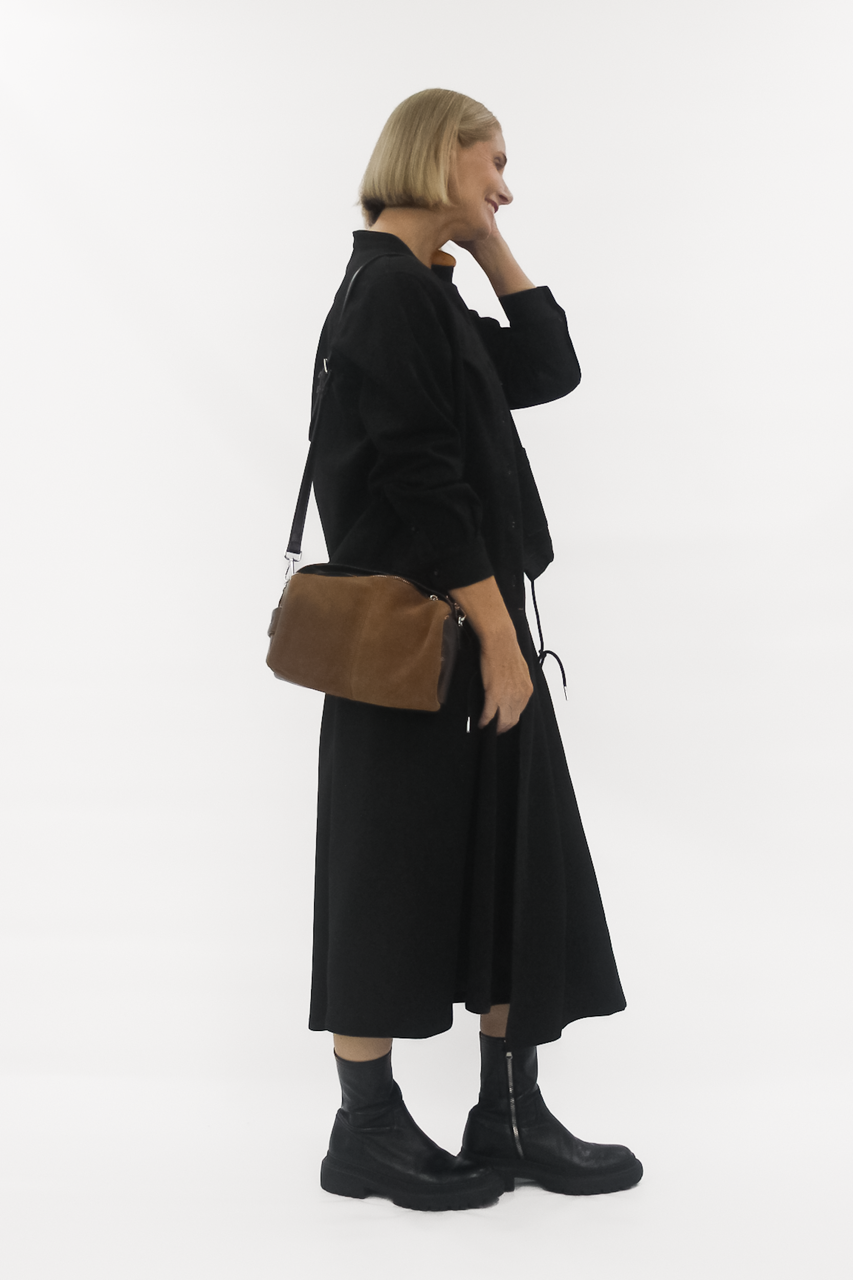 Woman wearing a black coat and holding a brown bag on a white background
