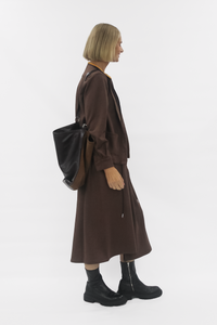 Person wearing a brown coat and carrying a black backpack on a white background