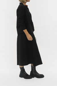 Person wearing a black outfit with a long dress and jacket on a white background